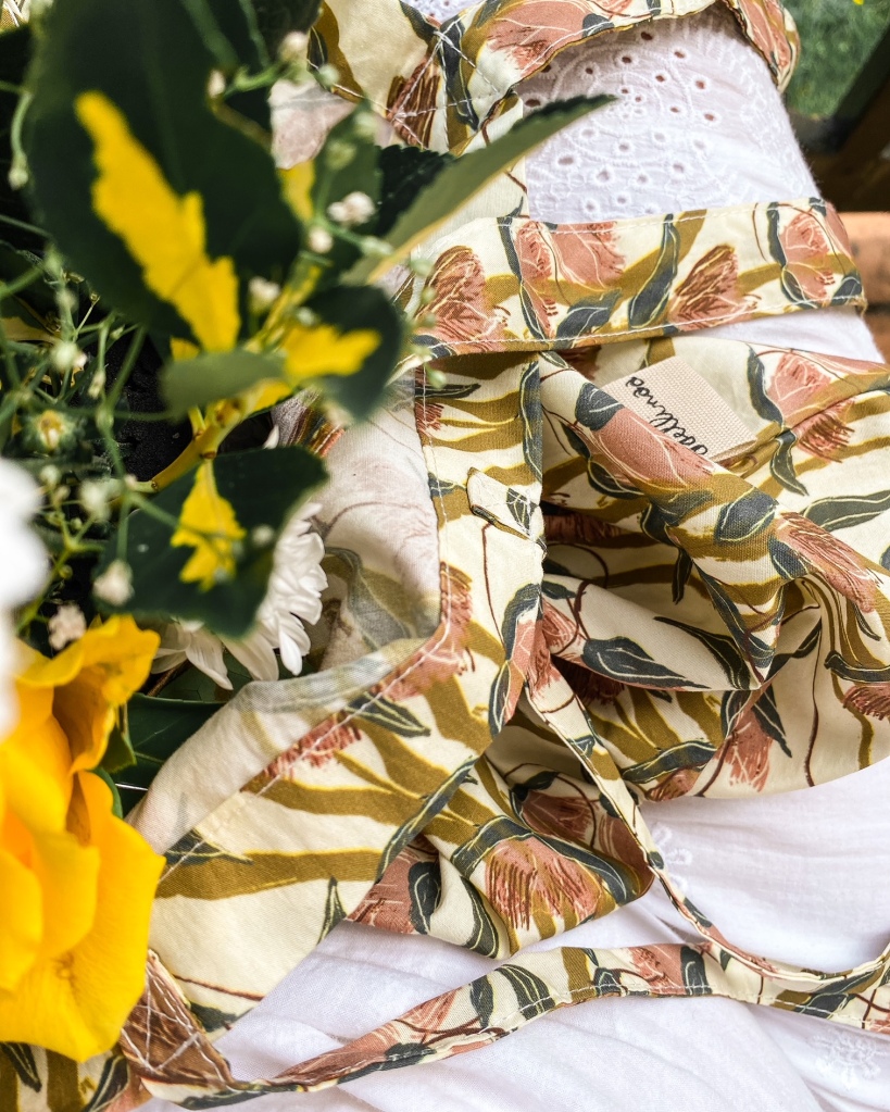Sac à fleurs dont sortent des fleurs jaunes sur les genoux d'une femme en robe blanche
