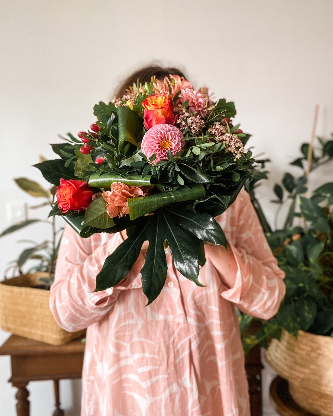 Femme en tunique rose se cachant le visage derrière un bouquet de fleurs