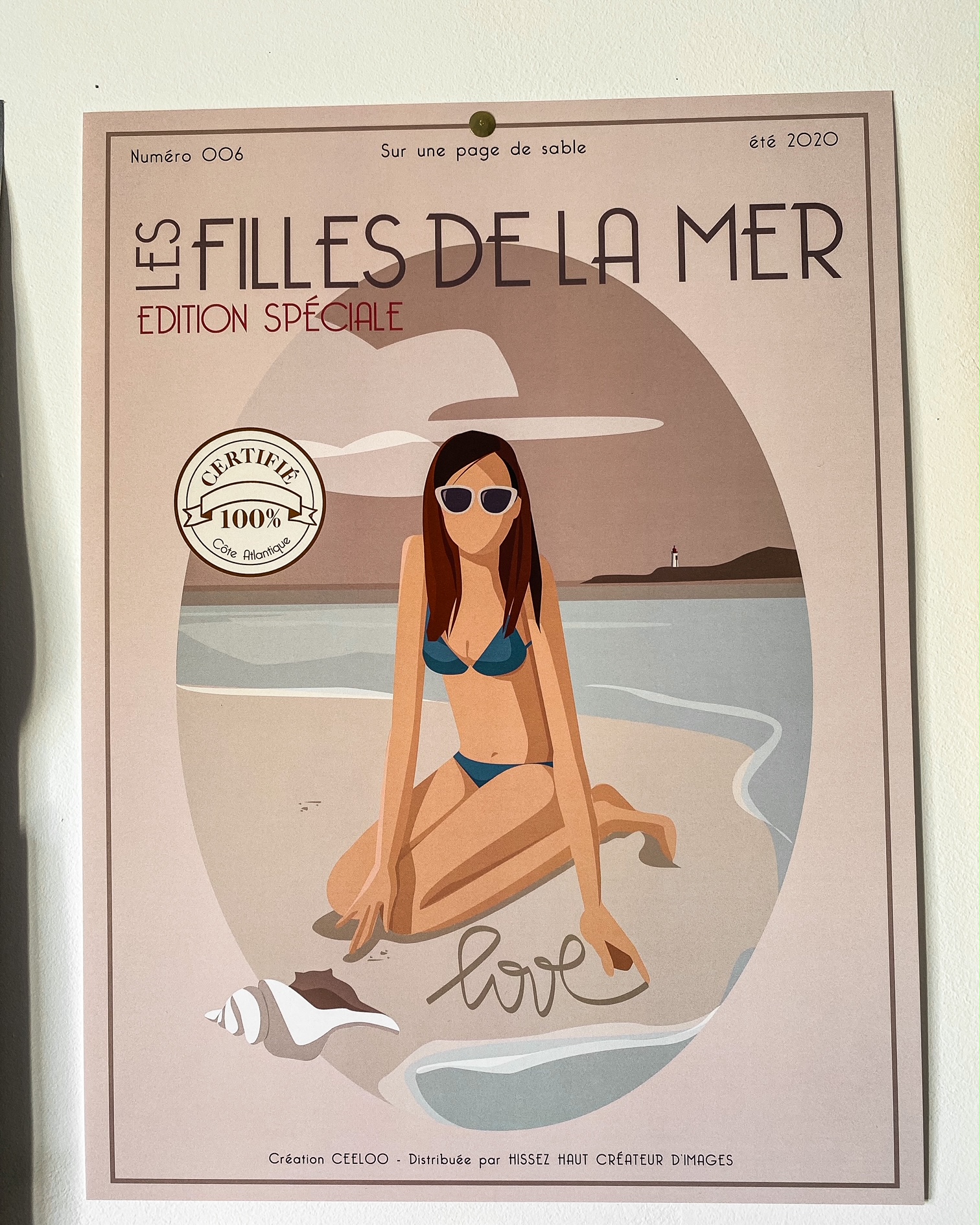 Une affiche "les filles de la mer" ; dessin d'une femme brune en maillot de bain assise sur une plage ; elle a écrit "love" sur le sable