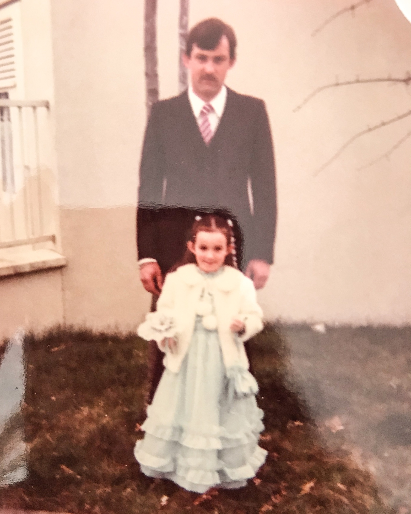 Une petite fille en robe longue avec derrière son papa en costume